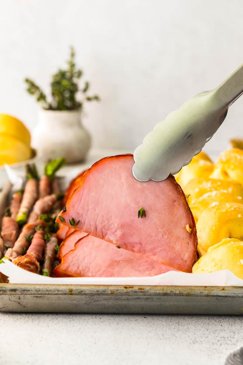 tongs grabbing a slice of brown sugar ham.