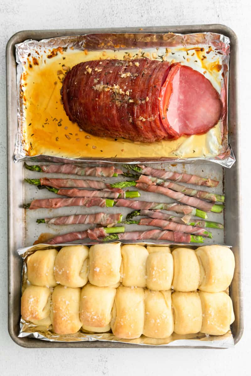 ham, prosciutto wrapped asparagus, and rolls on a sheet pan after baking
