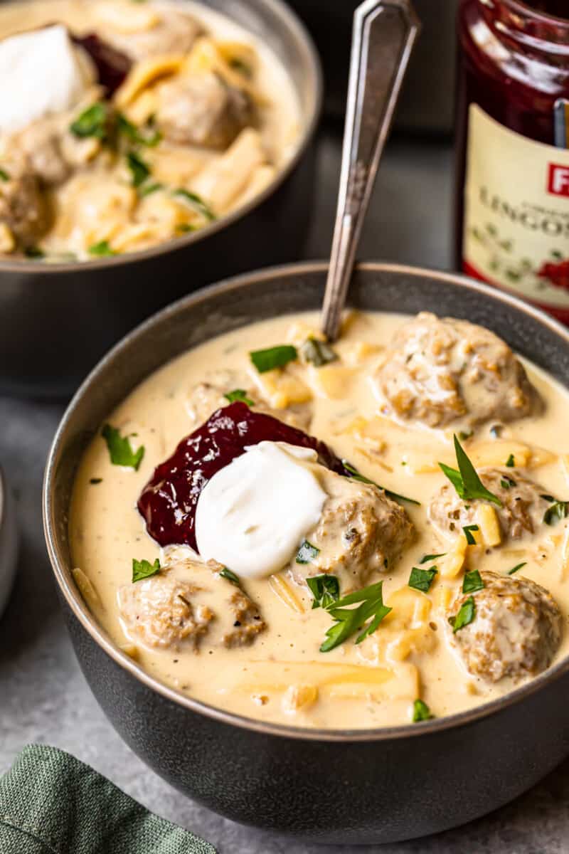 swedish meatball soup topped with sour cream and lingonberry jam in a bowl with a spoon