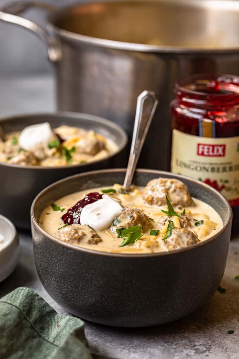 swedish meatball soup topped with sour cream and lingonberry jam in a bowl with a spoon