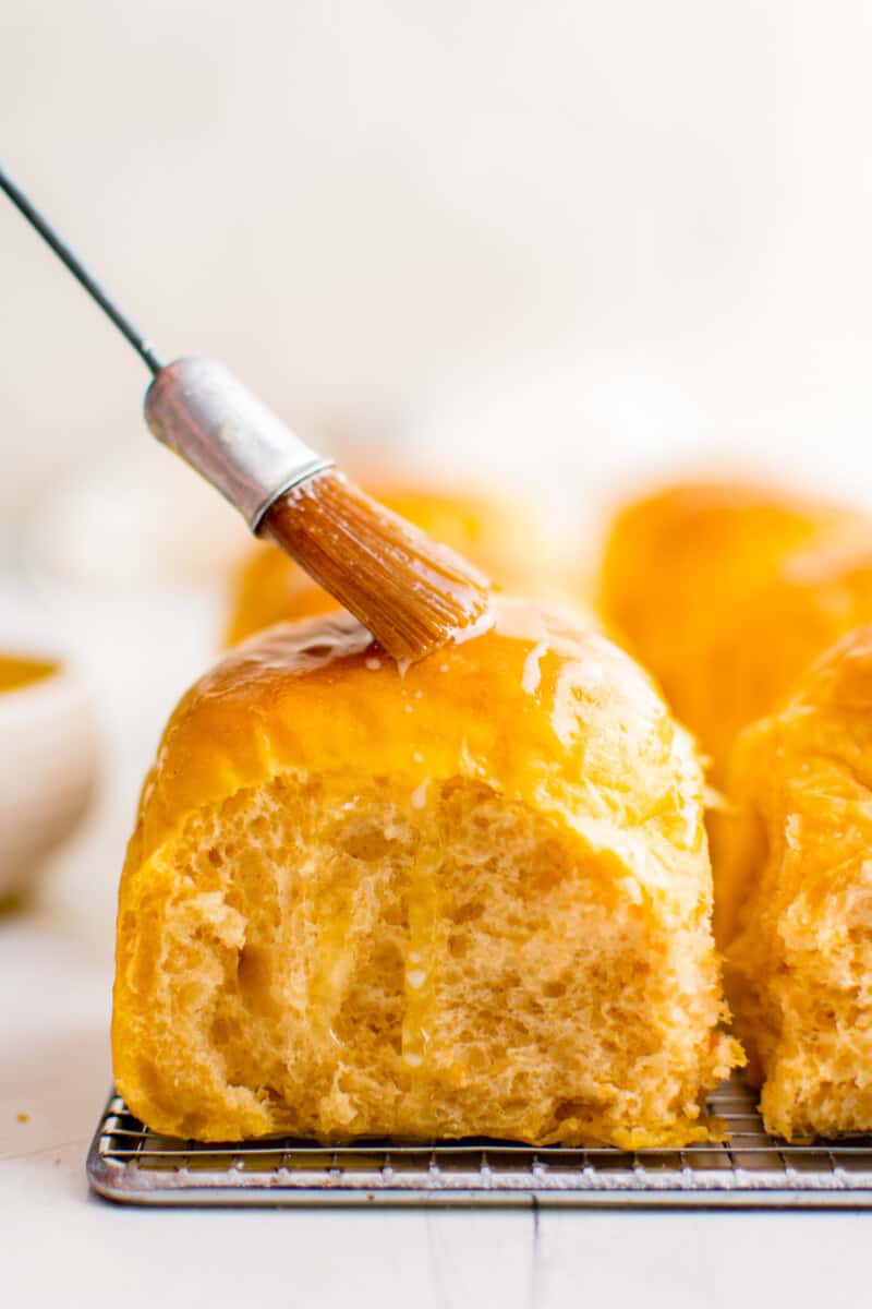 brushing melted butter onto sweet potato rolls