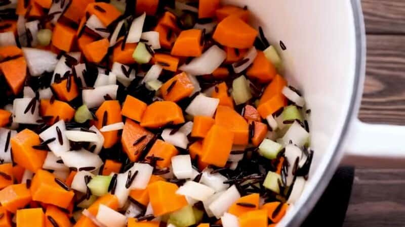 sliced carrots, onions, and celery in a large pot with grains of black wild rice