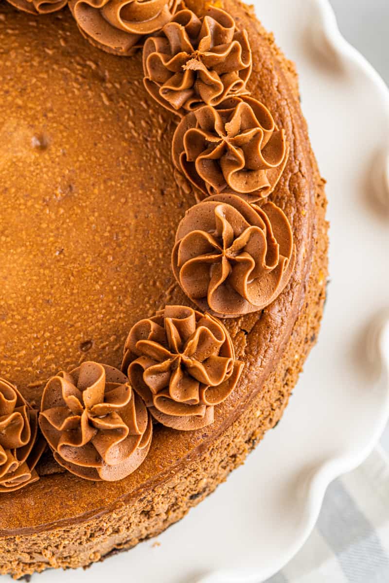 overhead image of chocolate cheesecake topped with swirls of whipped chocolate frosting on a white cake stand