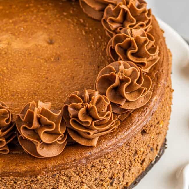 chocolate cheesecake topped with swirls of whipped chocolate frosting on a white cake stand