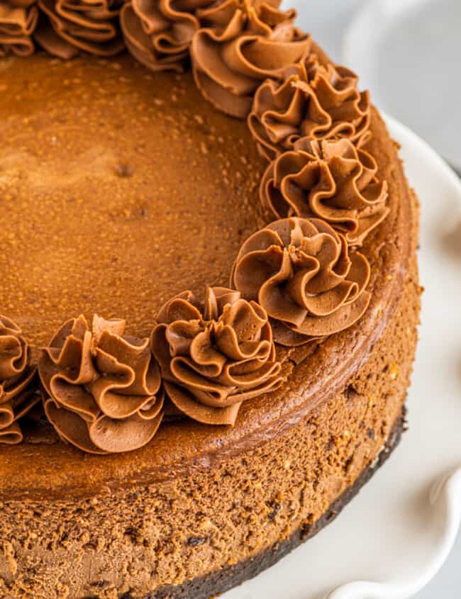 chocolate cheesecake topped with swirls of whipped chocolate frosting on a white cake stand