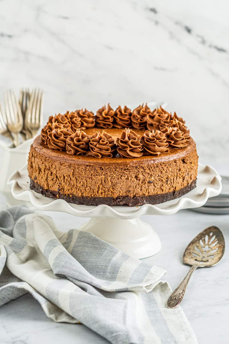chocolate cheesecake topped with swirls of whipped chocolate frosting on a white cake stand
