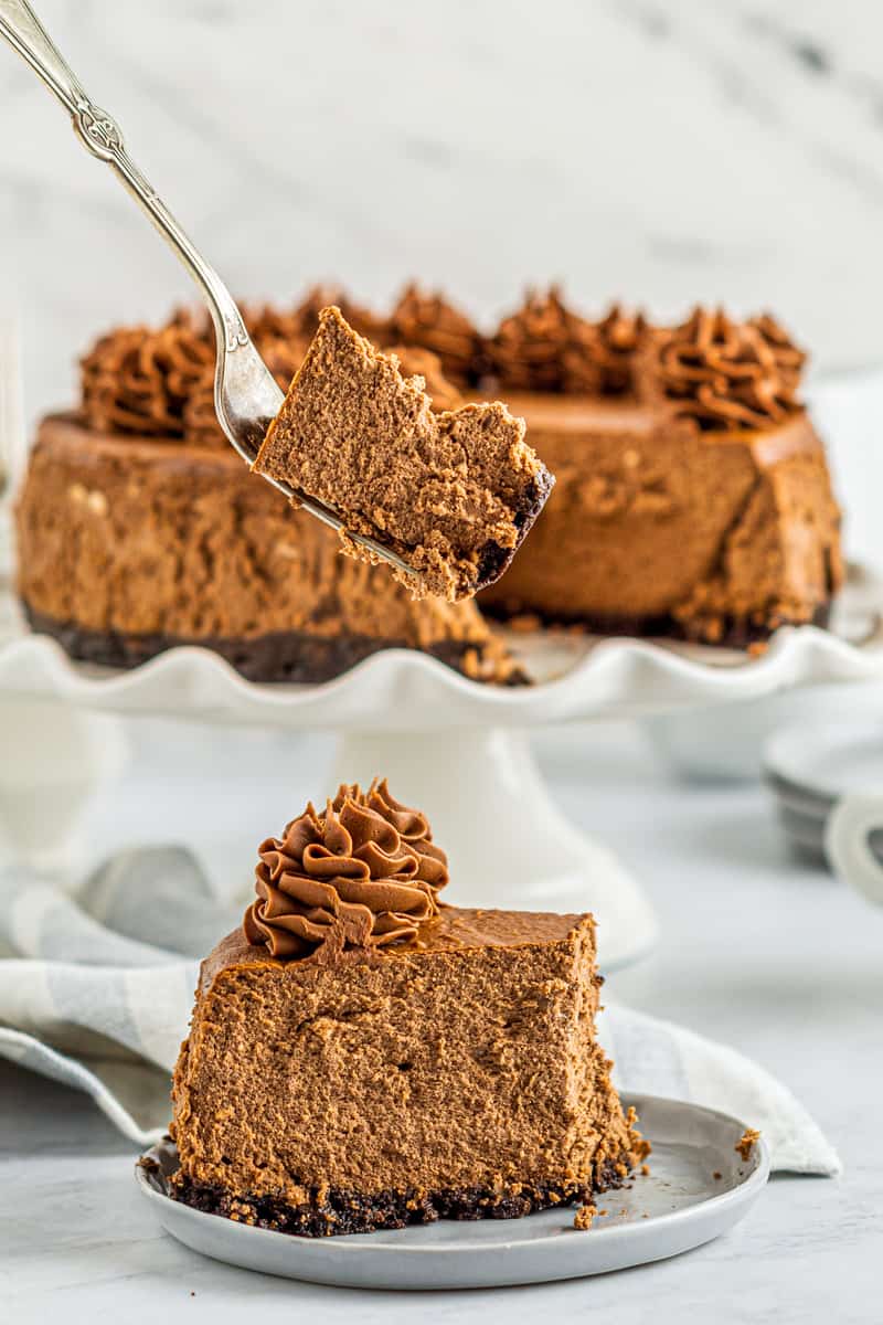 slice of chocolate cheesecake on a plate with a fork with a bite of chocolate cheesecake on it