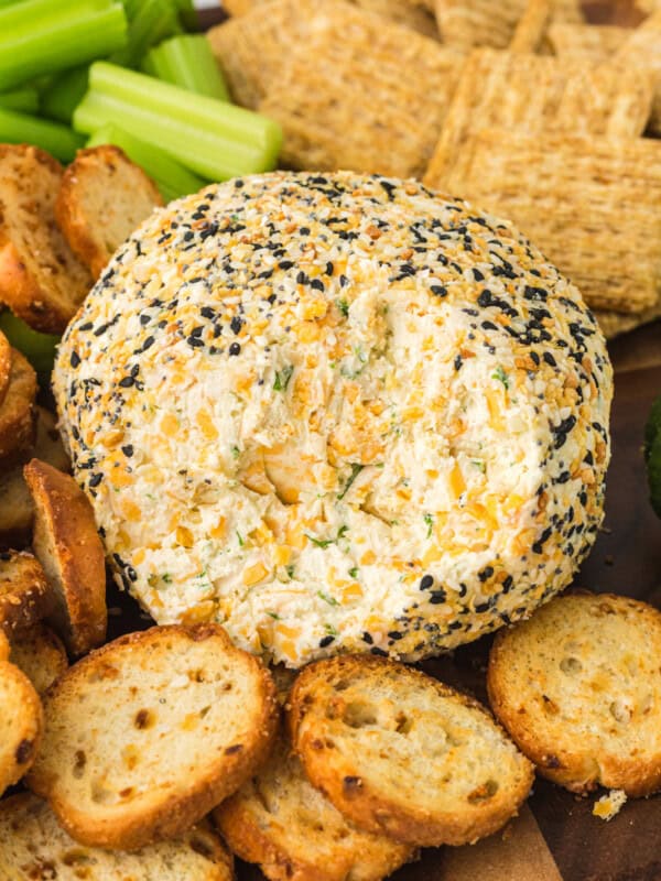 everything bagel cheeseball on a serving board with crackers, sliced cucumbers, and celery sticks with some of the cheeseball gone