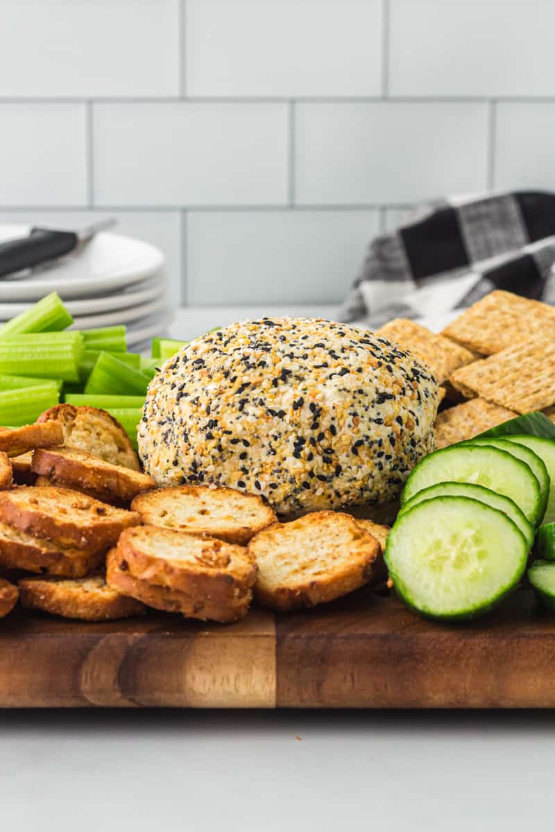 everything bagel cheeseball on a serving board with crackers, sliced cucumbers, and celery sticks ready for serving