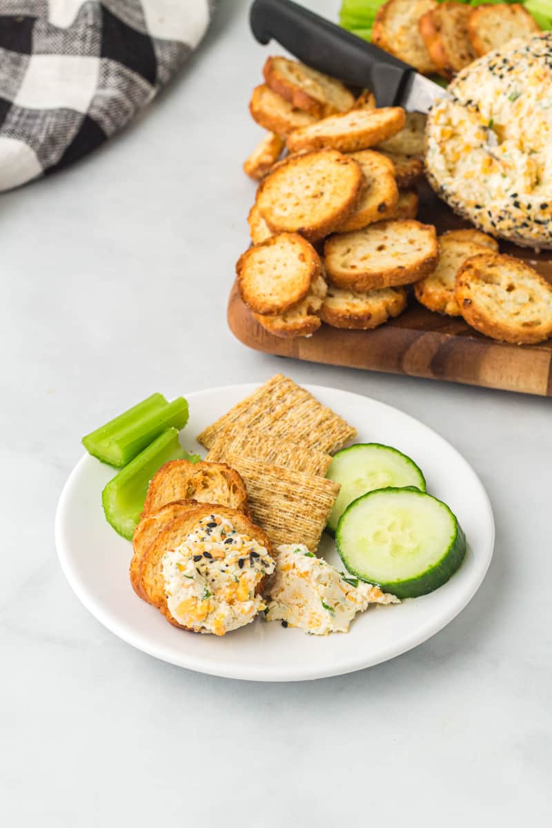 serving of everything bagel cheeseball, crackers, sliced cucumbers, and celery sticks on a white appetizer plate