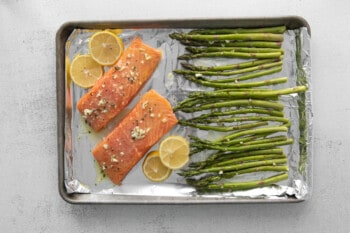 two salmon fillets with lemon slices and asparagus on a baking sheet.