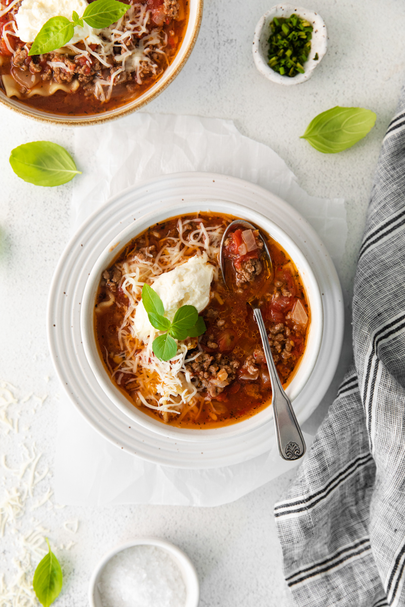 lasagna soup topped with ricotta cheese, parmesan cheese, and basil in a white bowl