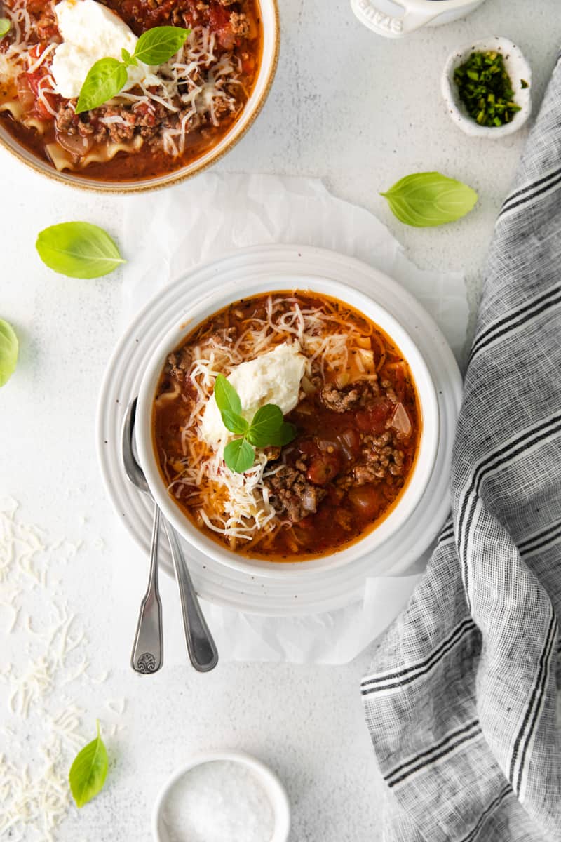 lasagna soup topped with ricotta cheese, parmesan cheese, and basil in a white bowl