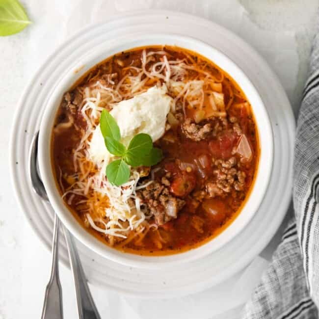 lasagna soup topped with ricotta cheese, parmesan cheese, and basil in a white bowl