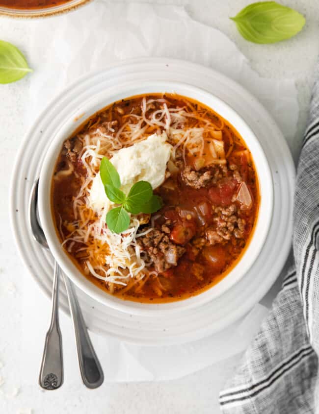 lasagna soup topped with ricotta cheese, parmesan cheese, and basil in a white bowl