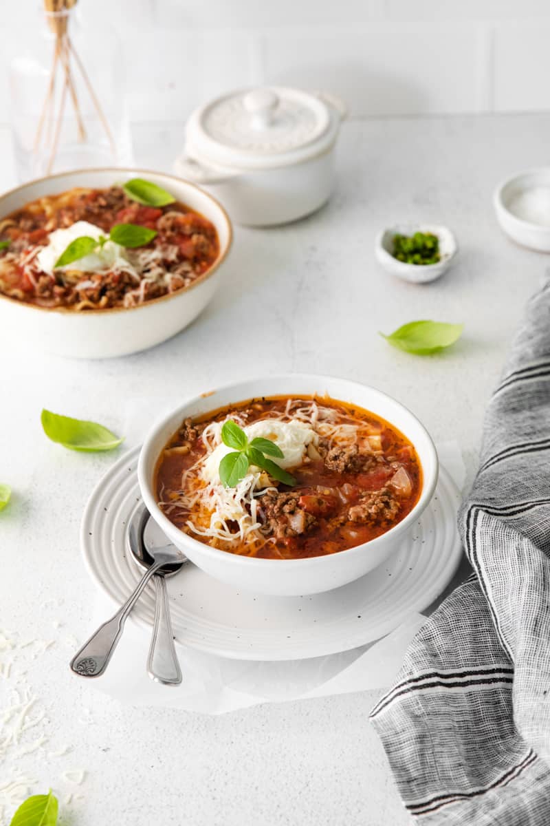 lasagna soup topped with ricotta cheese, parmesan cheese, and basil in a white bowl