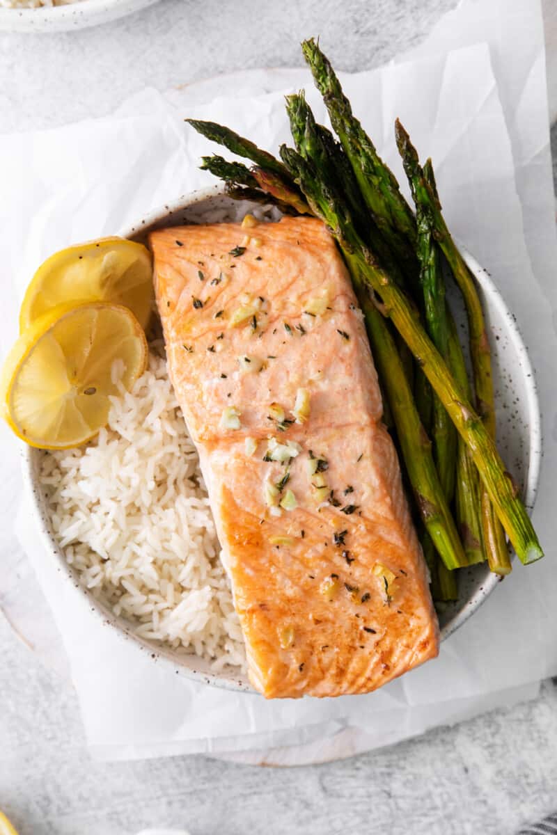 sheet pan lemon salmon on a bed of rice with asparagus in a white bowl.