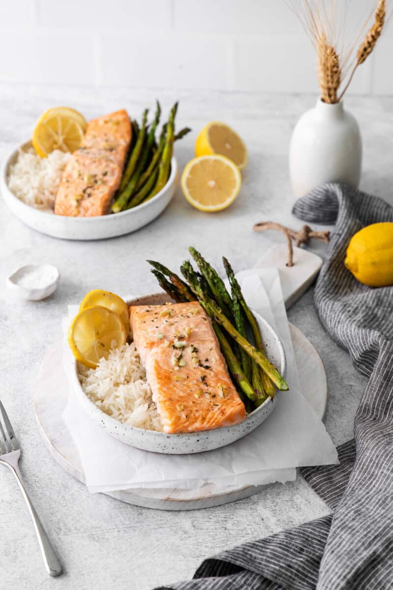 two white bowls of sheet pan lemon salmon on beds of rice with asparagus.