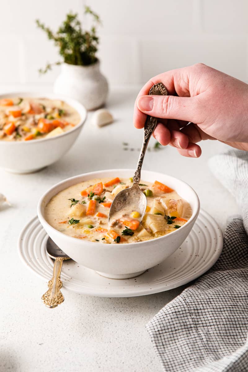 hand holding a spoon in a bowl of shepherd's pie soup