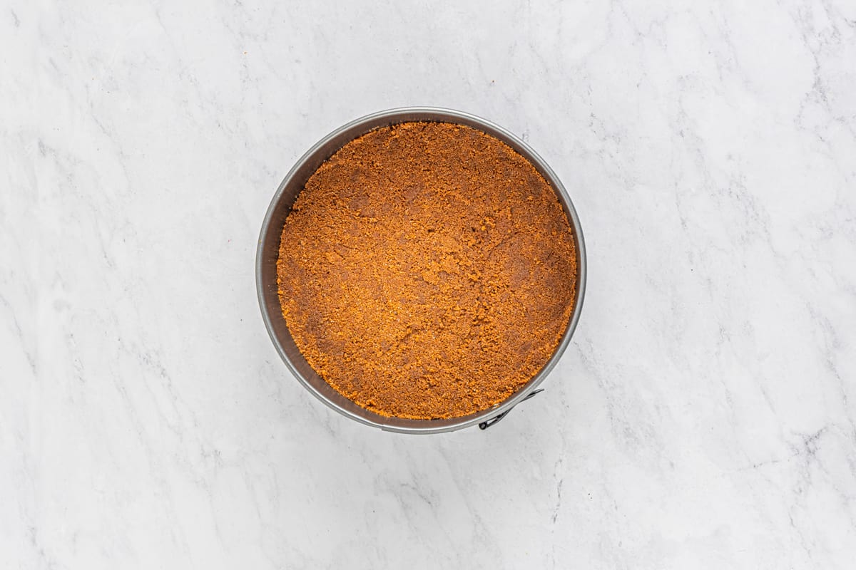 Biscoff cookie cheesecake crust in the bottom of a springform pan.