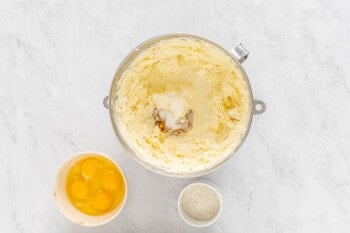 creamed sugar and cream cheese in a mixing bowl, 4 eggs in a white bowl, and flour in a white bowl