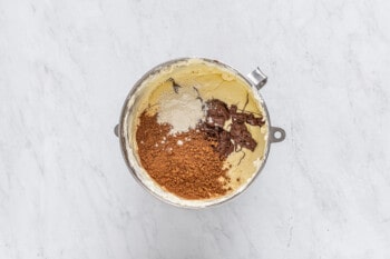 cocoa powder, melted chocolate, and flour added to cheesecake batter in a metal bowl