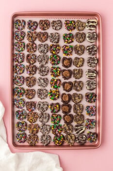 overhead image of chocolate covered pretzels with toppings on a baking sheet