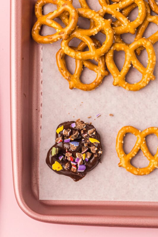 chocolate covered pretzel topped with crushed M&Ms on a baking sheet