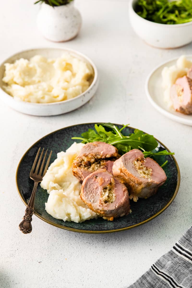 3 slices of stuffed pork loin, mashed potatoes, and salad on a black plate