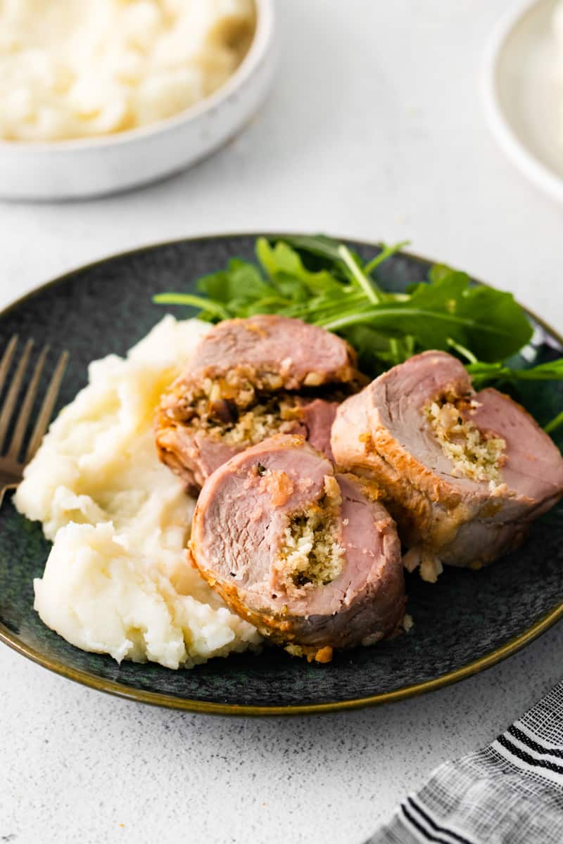 3 slices of stuffed pork loin, mashed potatoes, and salad on a black plate