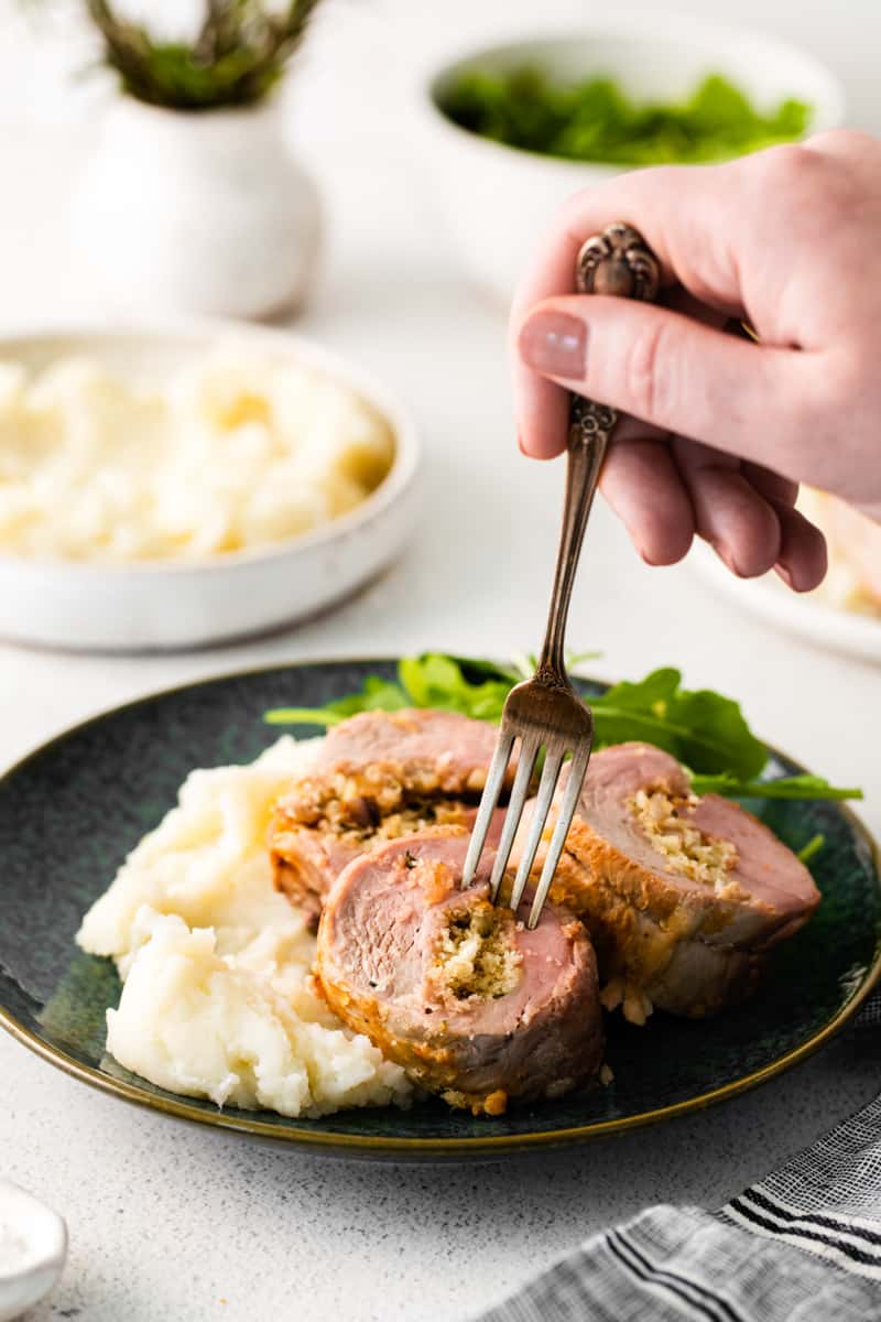 hand holding a fork in a piece of stuffed pork loin on a plate