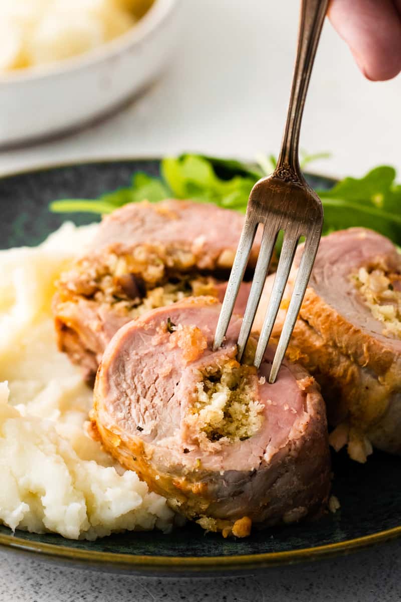 hand holding a fork in a piece of stuffed pork loin on a plate