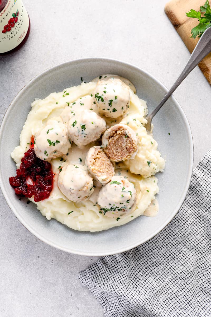 crockpot swedish meatballs on top of mashed potatoes in a bowl with a fork