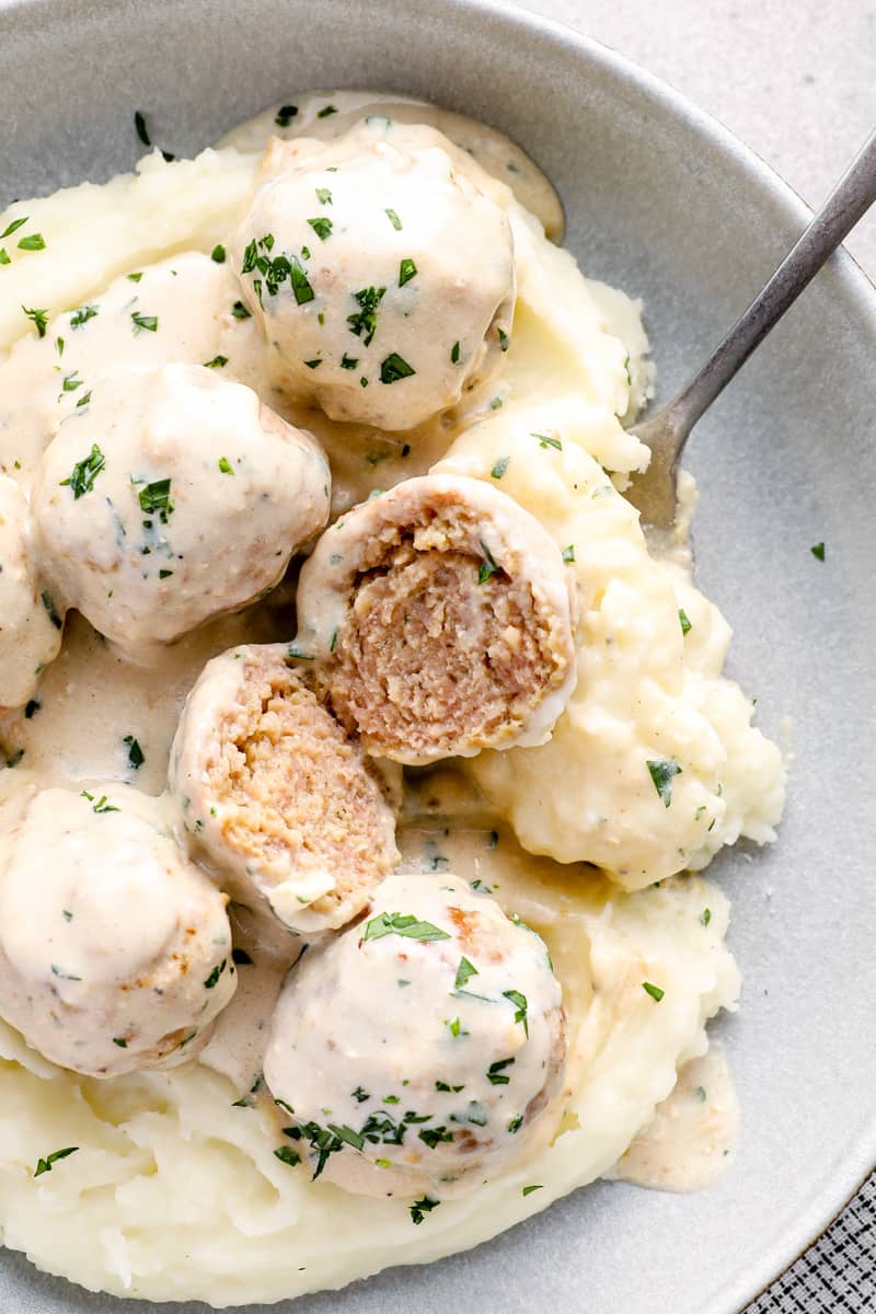 crockpot swedish meatballs on top of mashed potatoes in a bowl with a fork