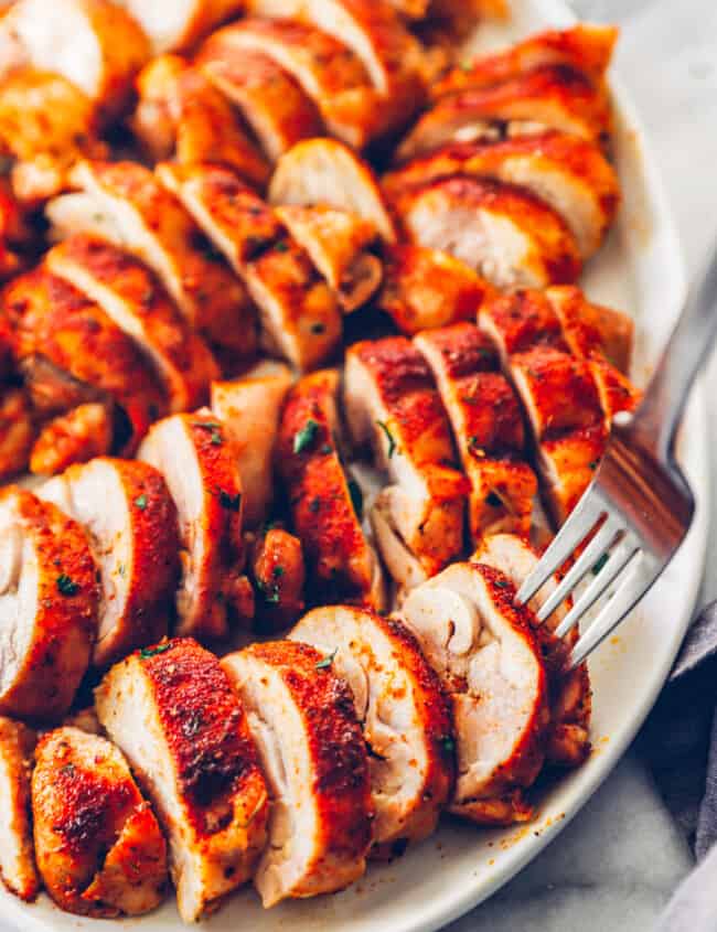 sliced baked chicken thighs on a white serving tray with a fork in one