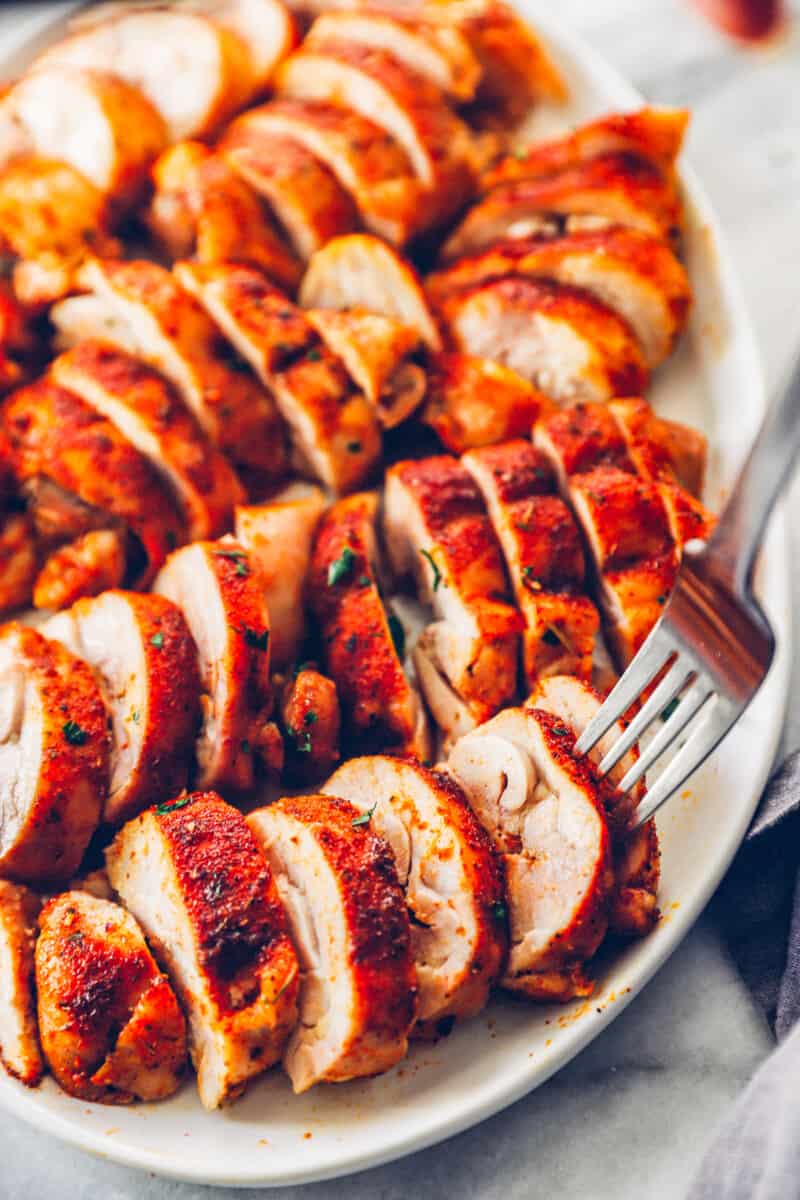 sliced baked chicken thighs on a white serving tray with a fork in one