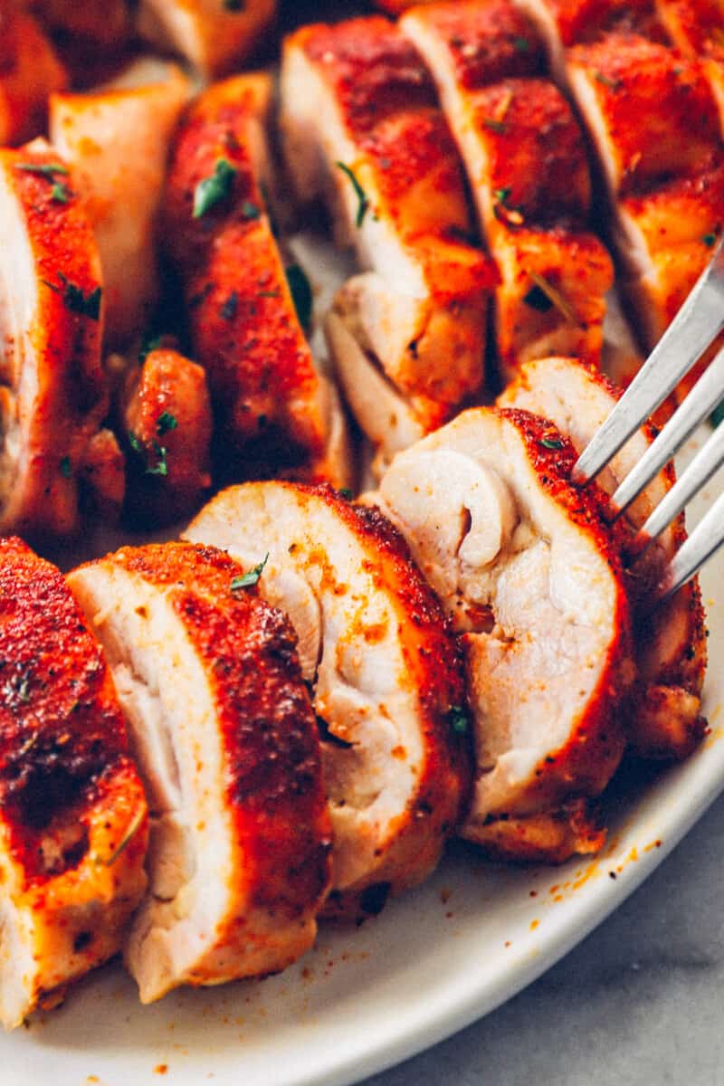 sliced baked chicken thighs on a white serving tray with a fork in one