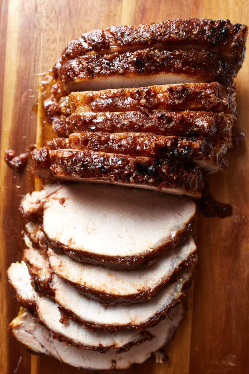 overhead view of sliced baked pork tenderloin on a cutting board.