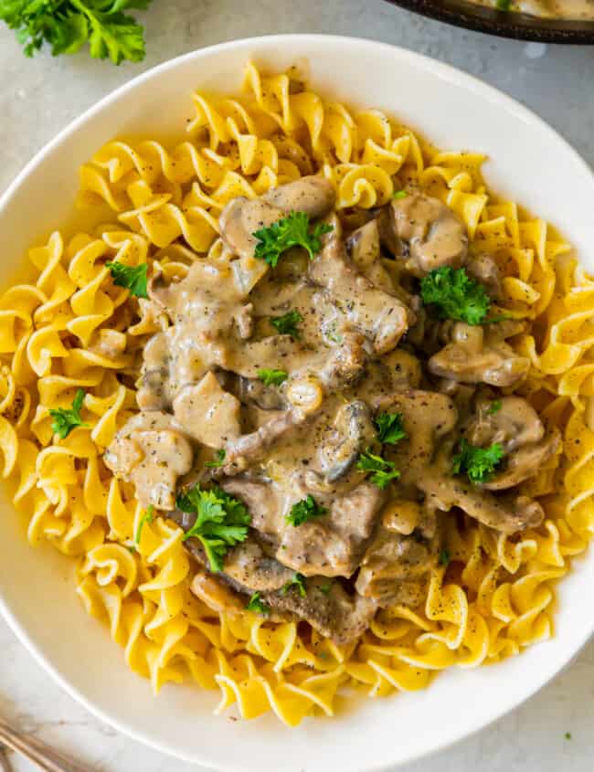 noodles topped with beef stroganoff in a white bowl