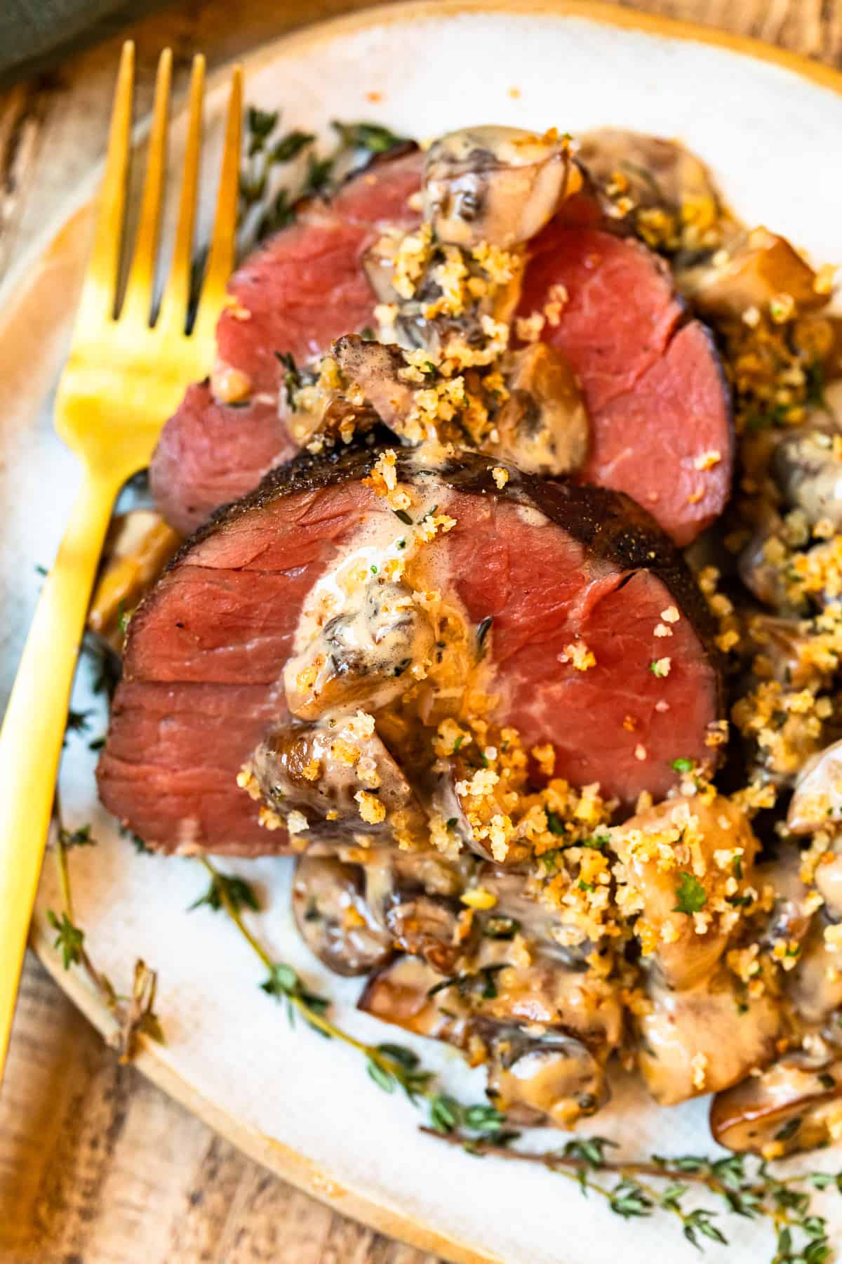 slices of beef tenderloin with mushroom sauce on a white plate with a fork