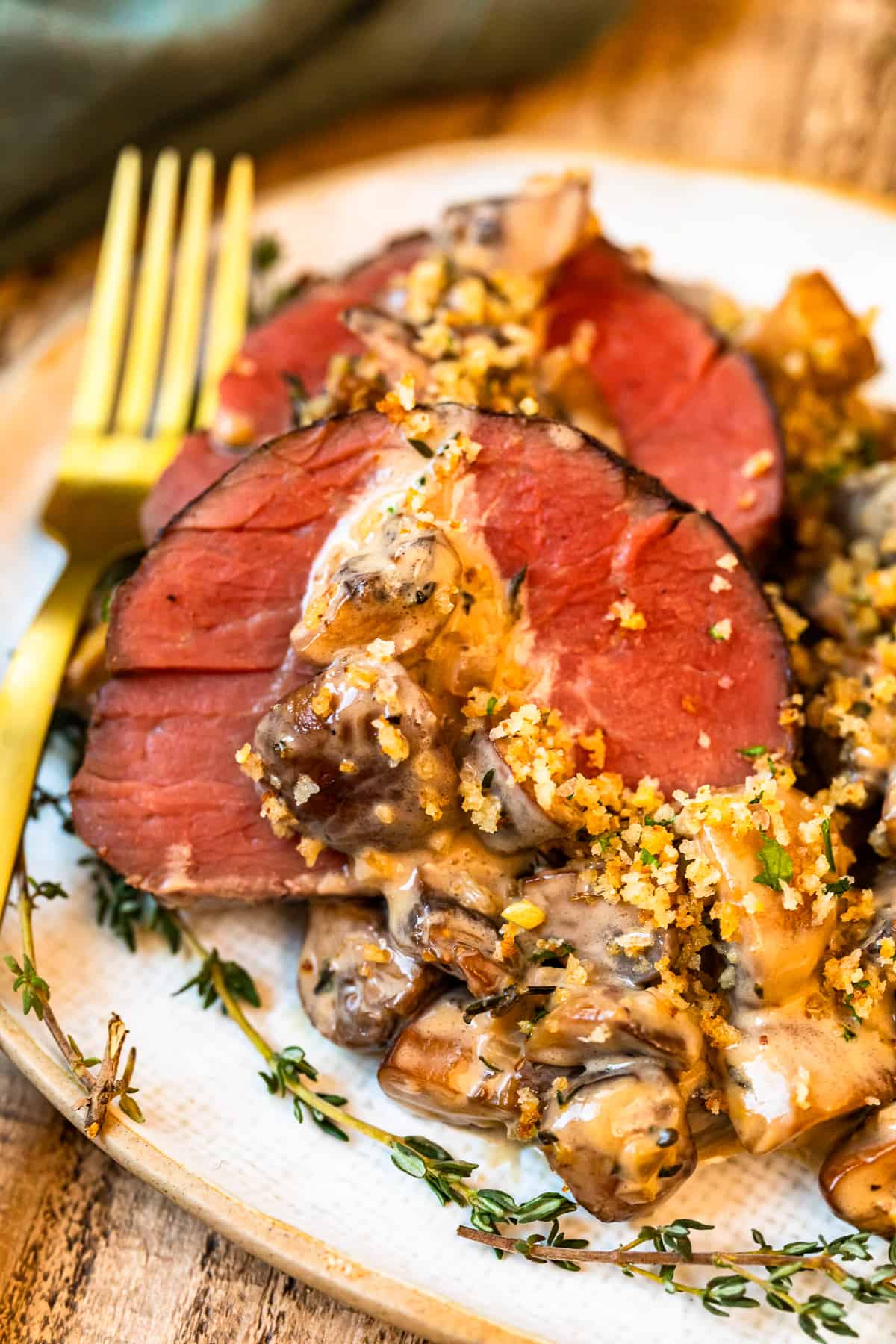 slices of beef tenderloin with mushroom sauce on a white plate with a fork