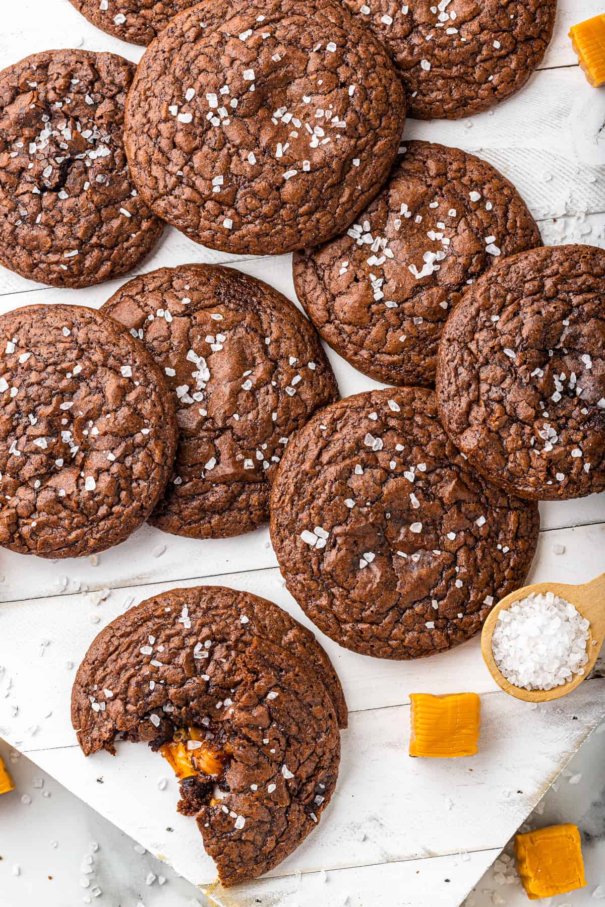 overhead image of chocolate brownie cookies topped with sea salt. one has a bite taken out, showing the caramel center.