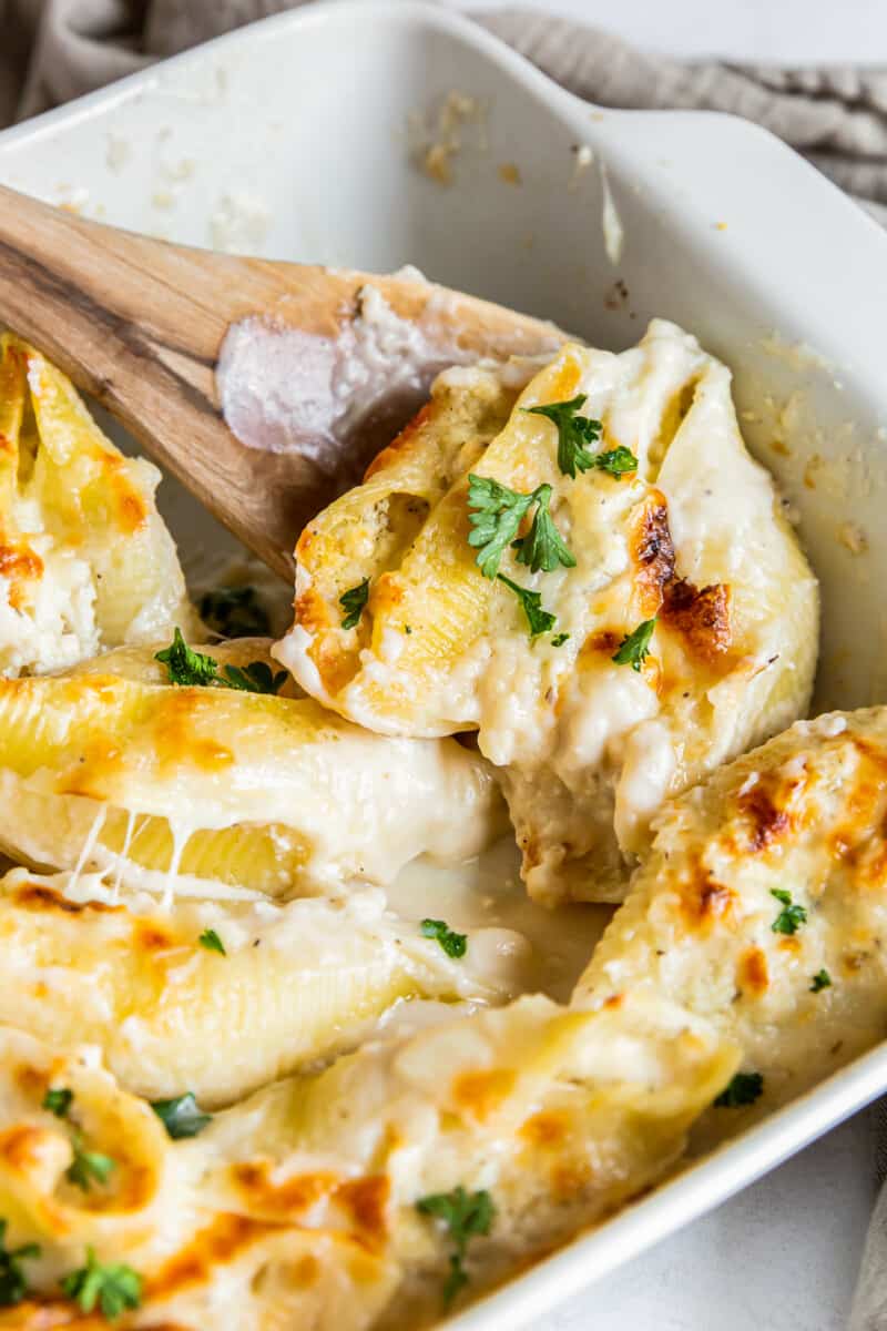 pasta shells stuffed with cheese and chicken topped with alfredo sauce in a baking dish with a wood spoon