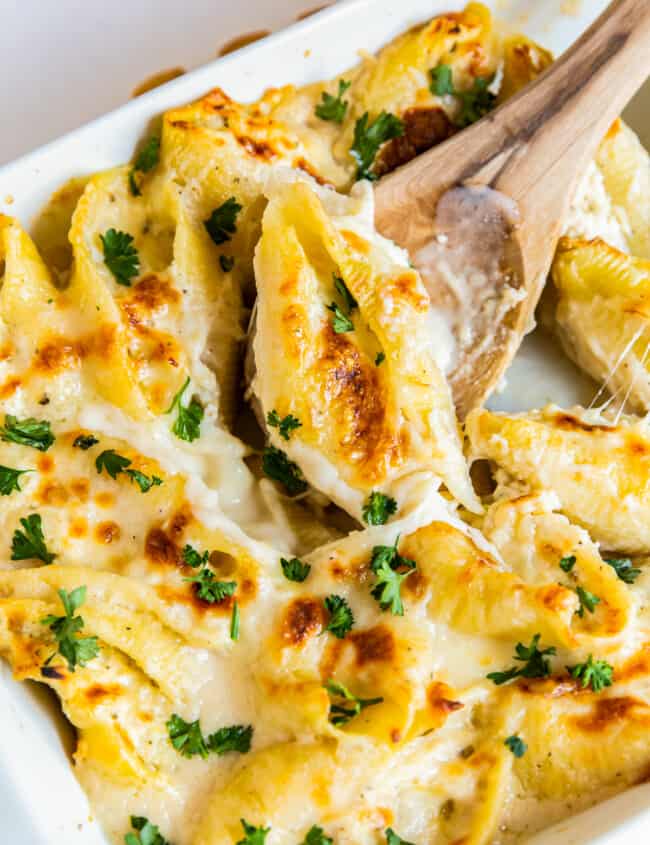 pasta shells stuffed with cheese and chicken topped with alfredo sauce in a baking dish with a wood spoon