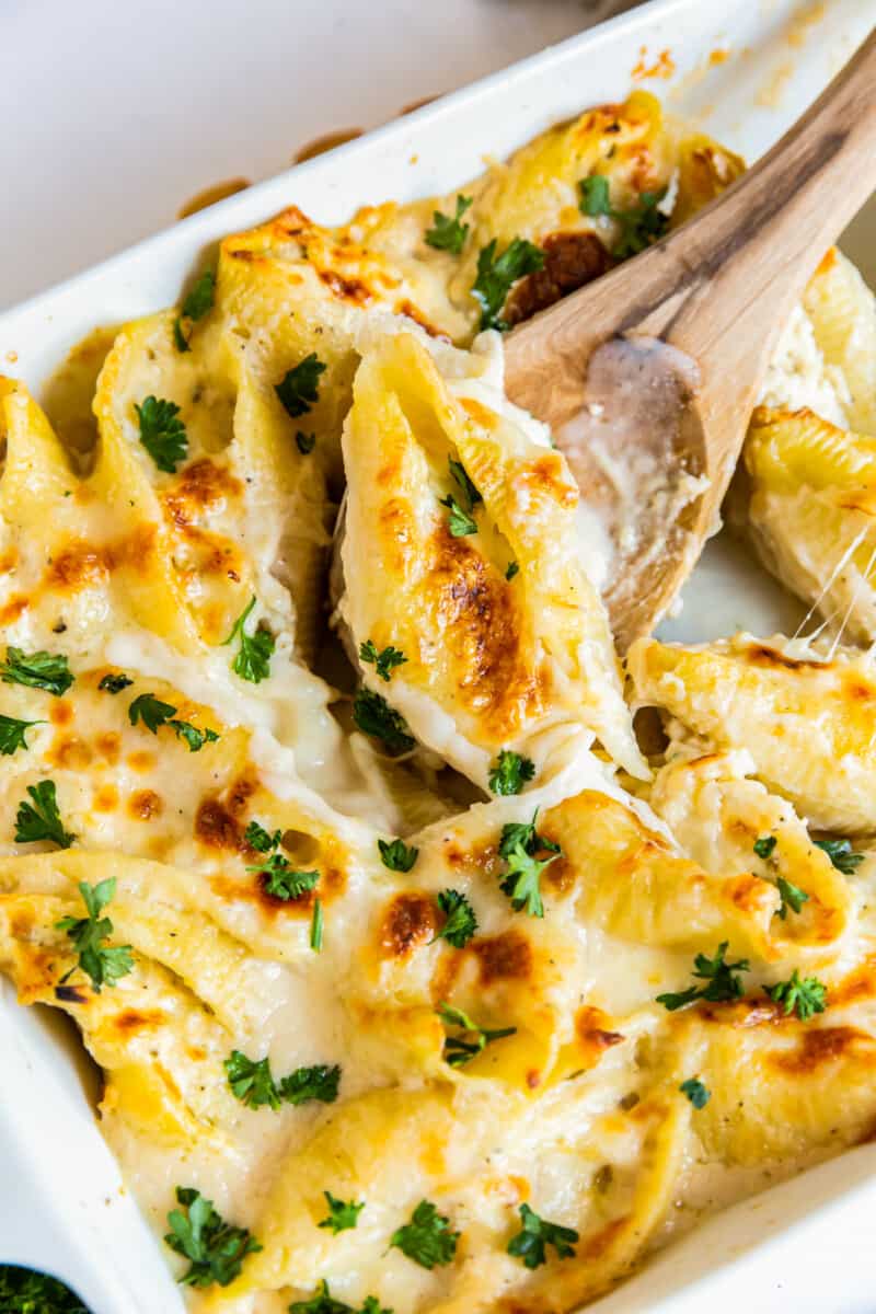 pasta shells stuffed with cheese and chicken topped with alfredo sauce in a baking dish with a wood spoon