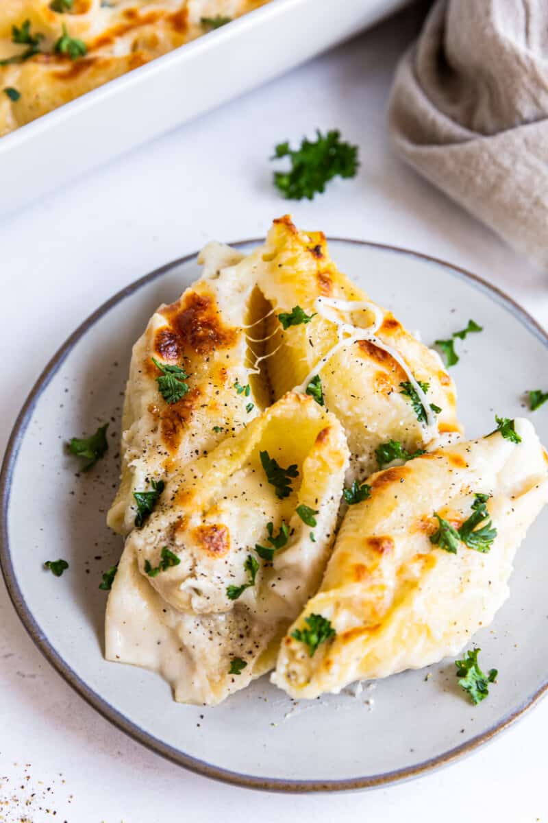 pasta shells stuffed with cheese and chicken topped with alfredo sauce on a white plate