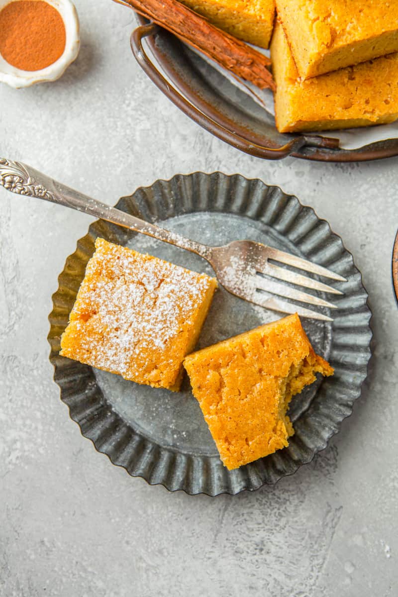 2 pieces of cornbread with a bite taken from one piece on a metal plate with a fork