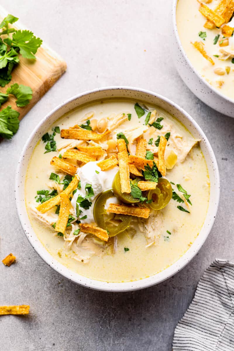 crockpot white chicken chili in white bowl garnished with cheese, jalapenos, and tortilla strips