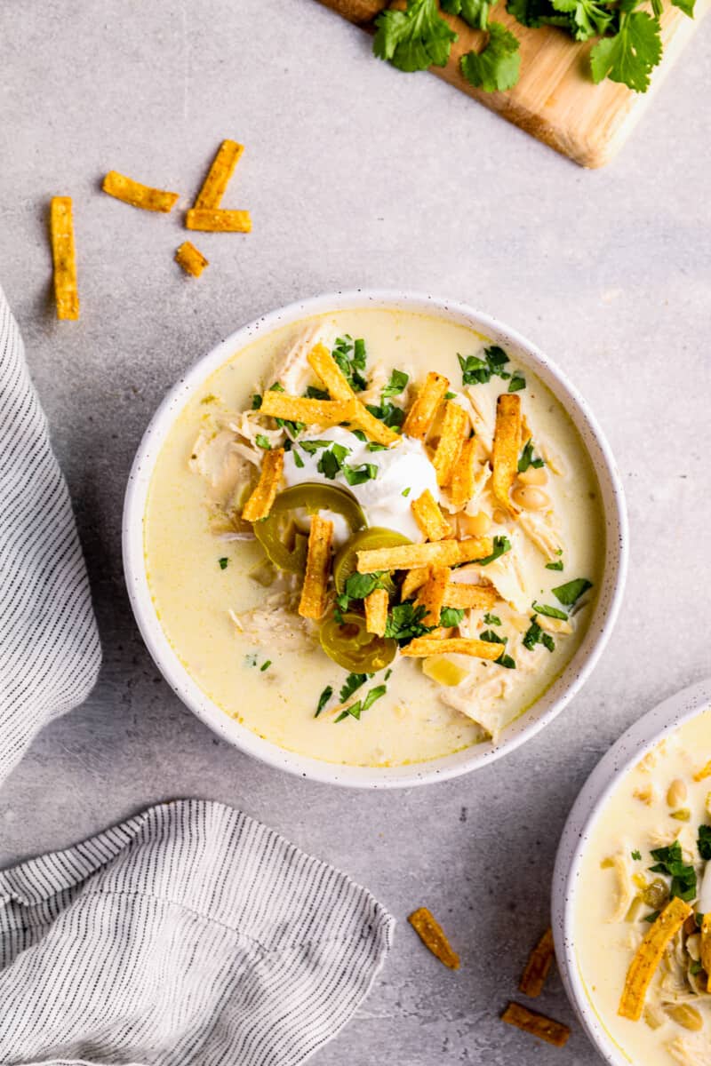 crockpot white chicken chili in white bowl garnished with cheese, jalapenos, and tortilla strips