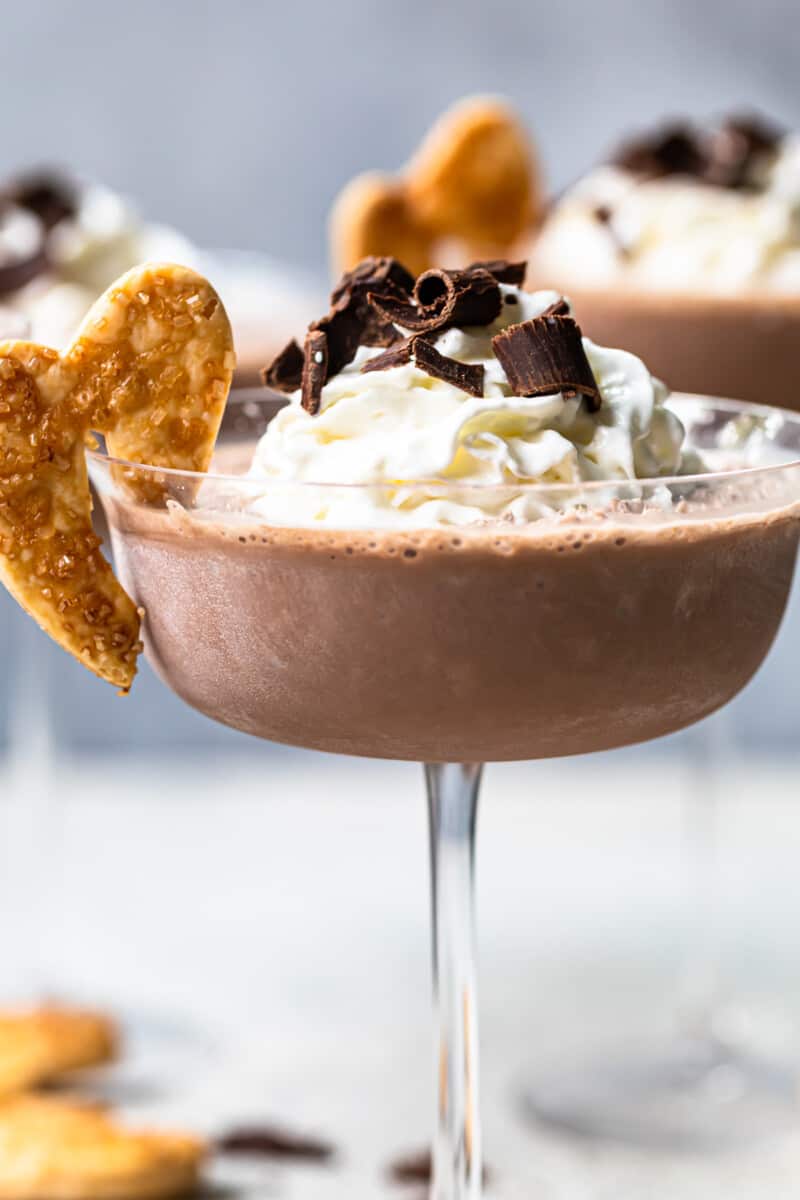 frozen french silk pie cocktail in a glass topped with whipped surf and chocolate shavings and garnished with baked pie husks cookie